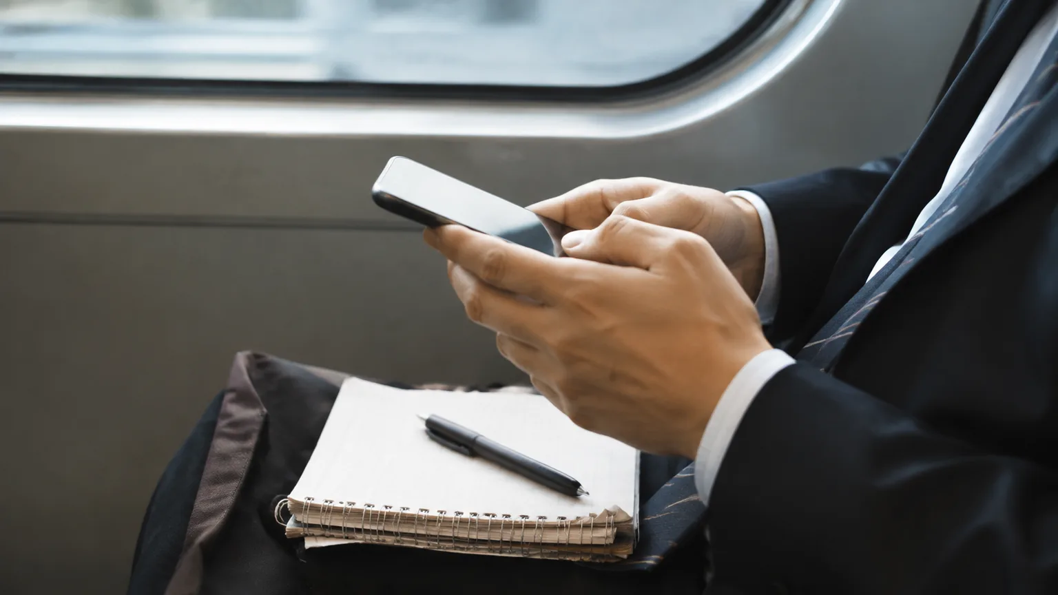 通勤中にスマートフォンとノートで学ぶ会社員の手元